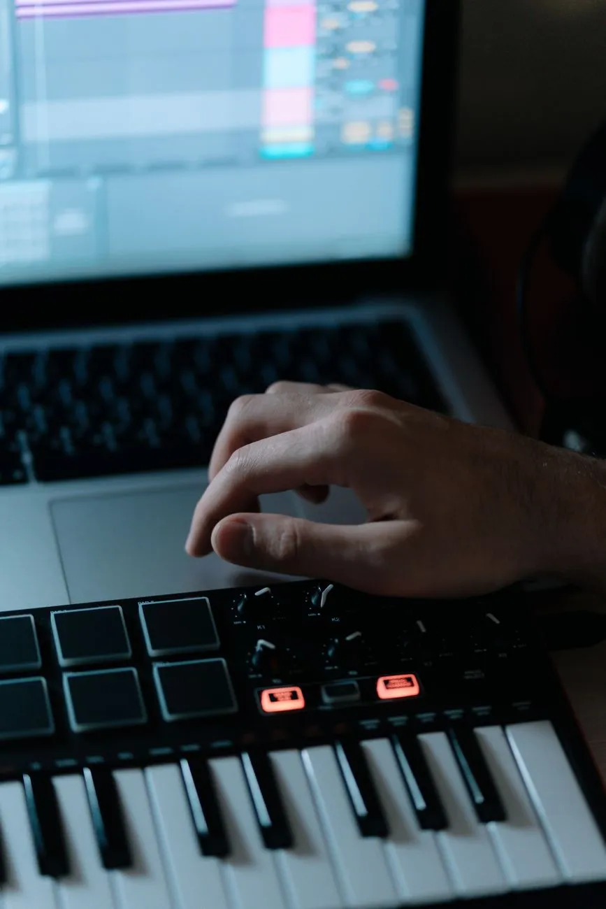 Close up of hand adjusting synthesizer controls with laptop screen displaying au